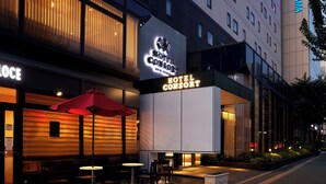 A hotel with a modern facade, outdoor seating area with tables and chairs, and a prominent sign for the hotel. - Hotel Consort Shin-Osaka (Osaka)