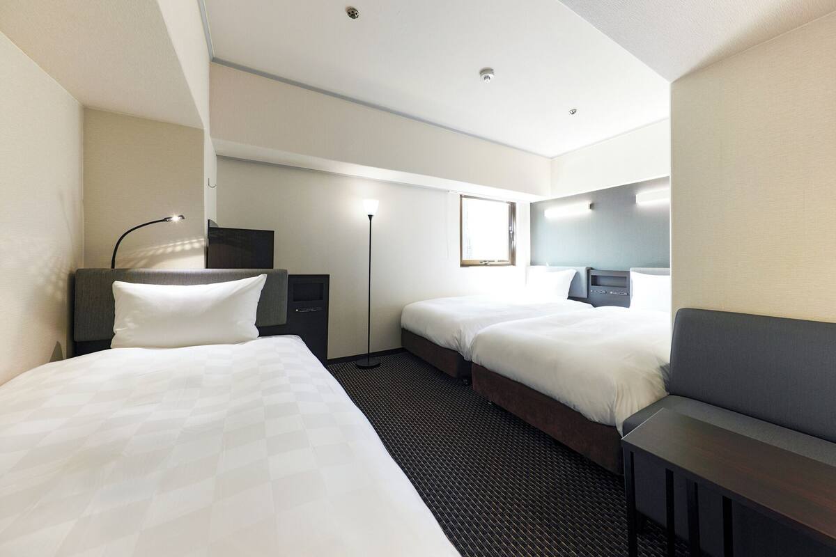 Hotellihuone, jossa on kaksi sänkyä, työpöytä, tuoli, pöytävalaisin, yöpöytä, peili ja ikkuna.