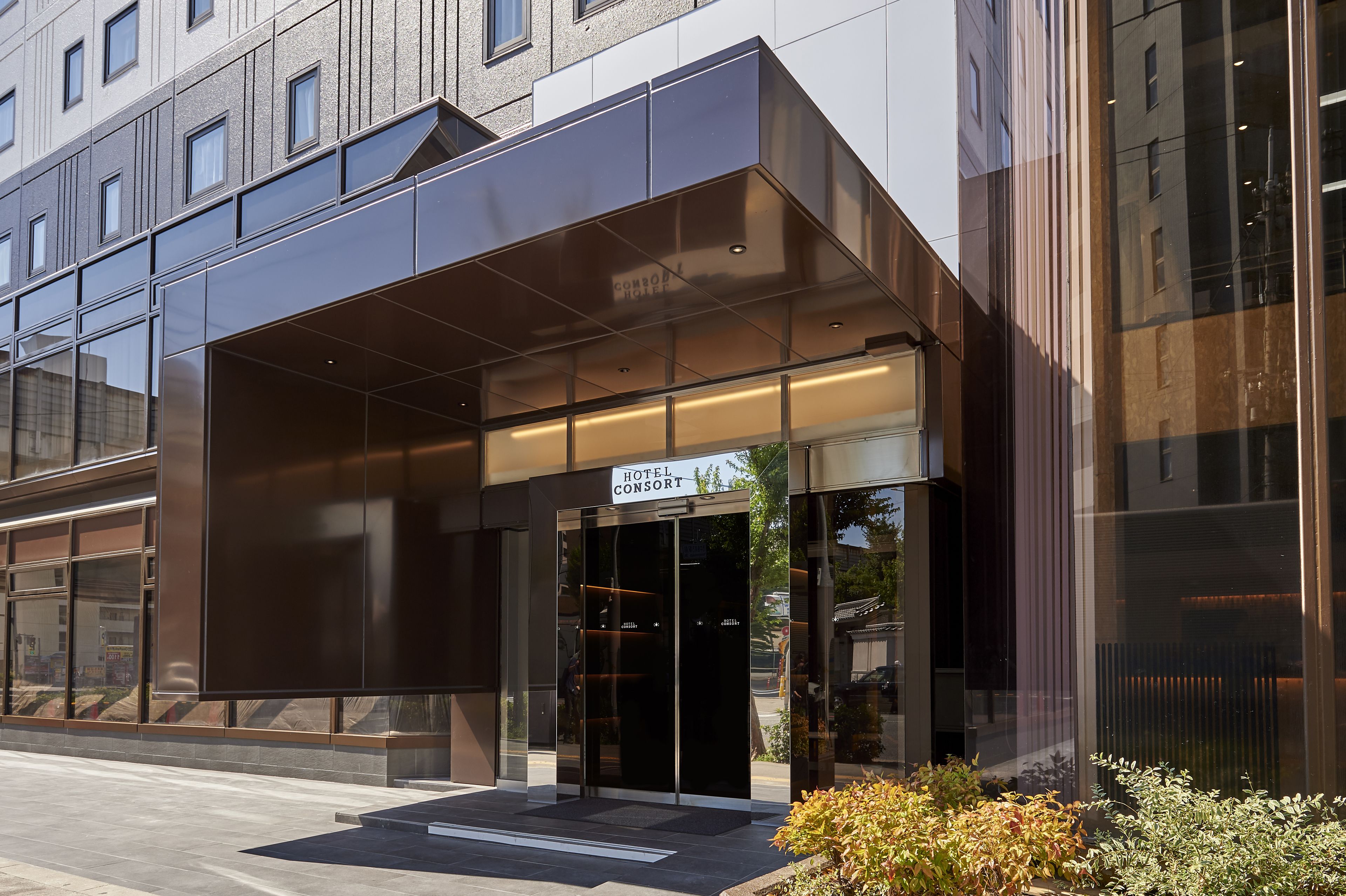 Una entrada de hotel moderna con fachada de vidrio, un dosel de entrada destacado y un letrero que dice "HOTEL CONSORT".