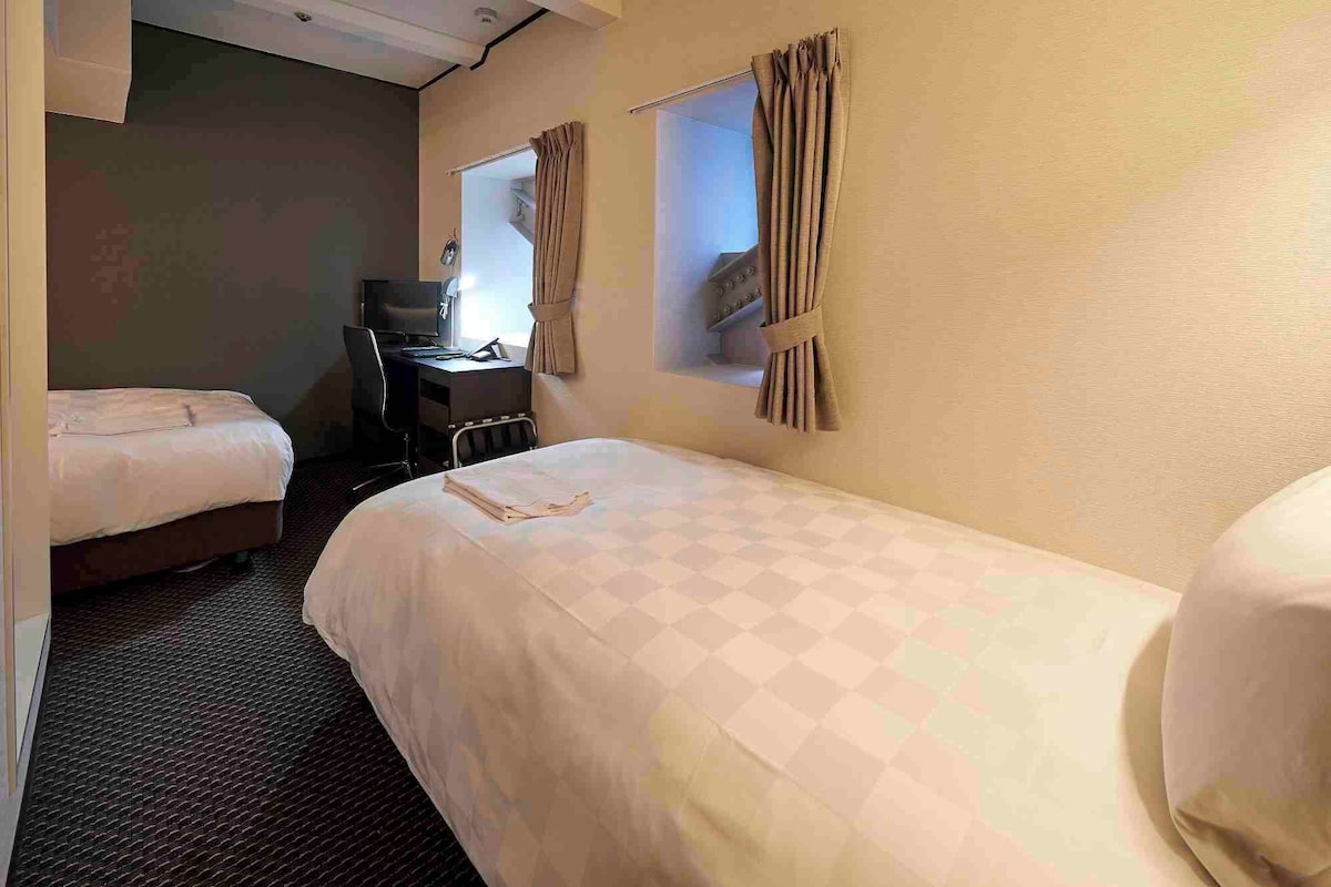 A hotel room with two beds, a desk, and a chair.