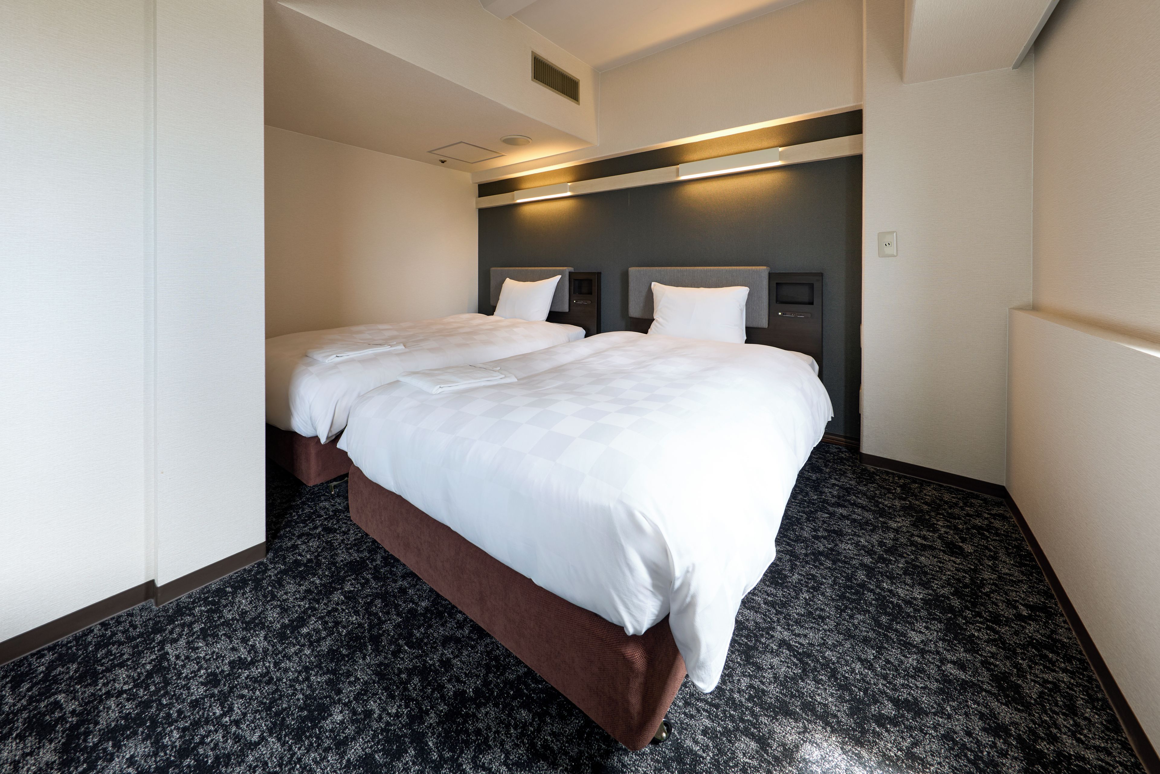 A hotel room with a large bed, a dark carpet, and a modern headboard.