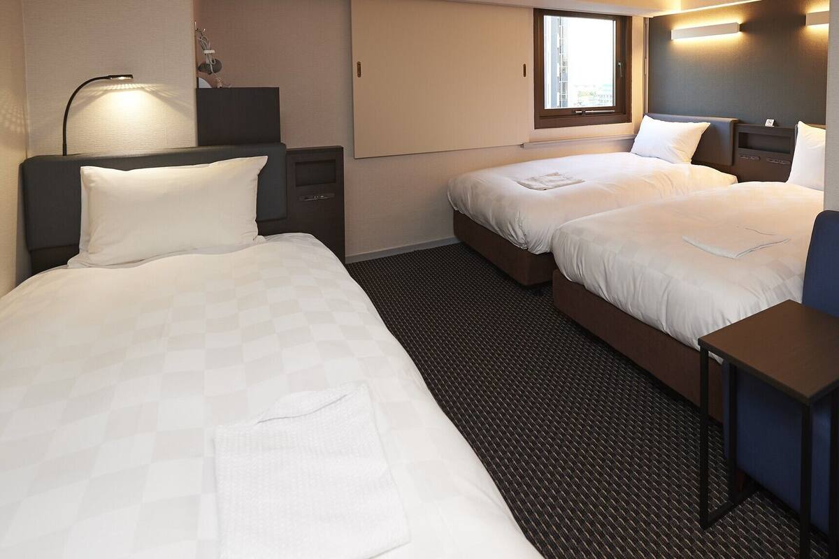 Hotellihuone, jossa on kaksi sänkyä, työpöytä, tuoli, lamppu ja ikkuna.