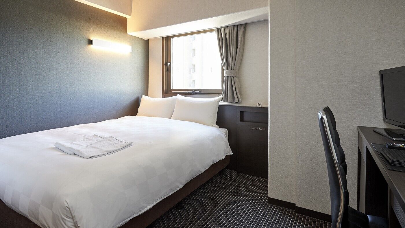 A hotel room with a bed, a desk, a chair, a television, and a window with curtains.