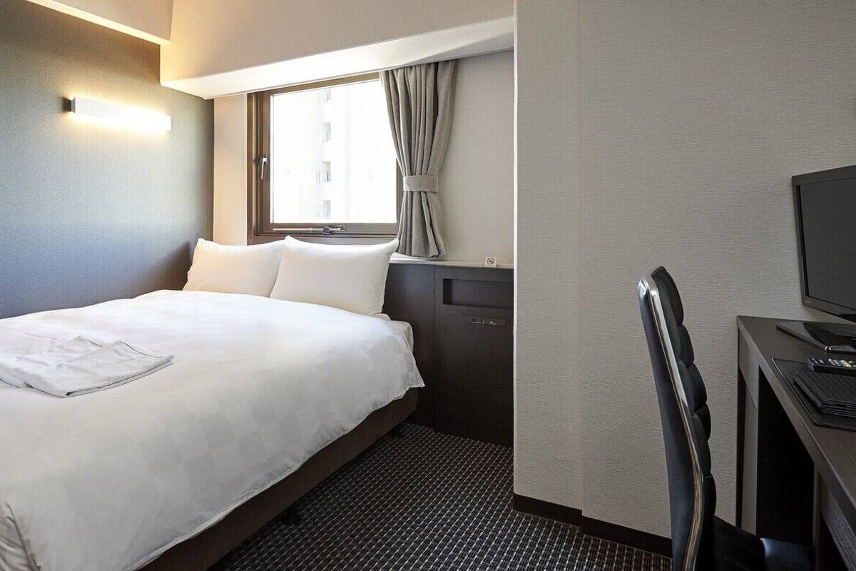 Une chambre d’hôtel équipée d’un lit, d’un bureau, d’une chaise, d’une télévision et d’une fenêtre avec des rideaux.