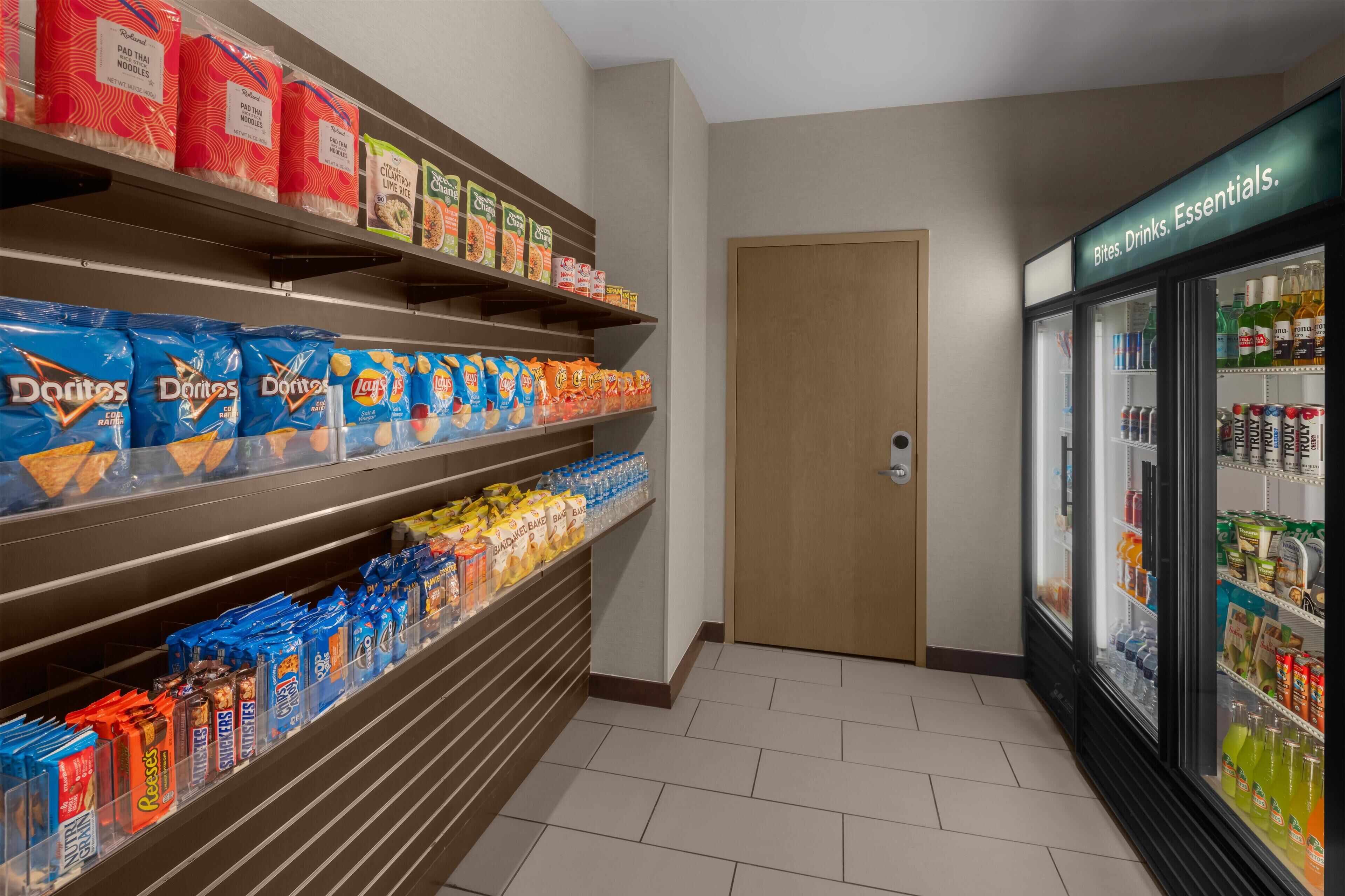 Ein Gang mit Regalen voller Snacks wie Doritos und Lay's, sowie ein Kühlbereich mit Getränken.
