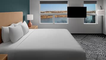 A hotel room with a large bed, two windows with a view of a lake, a flat-screen TV, and a lamp.