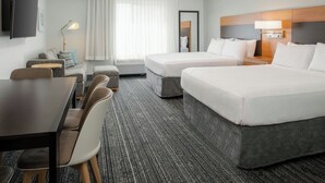 A hotel room with two beds, a desk, chairs, a TV, a lamp, and a window with curtains.