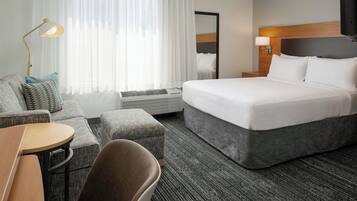 A hotel room with a bed, a sofa, a chair, a small table, and a lamp.