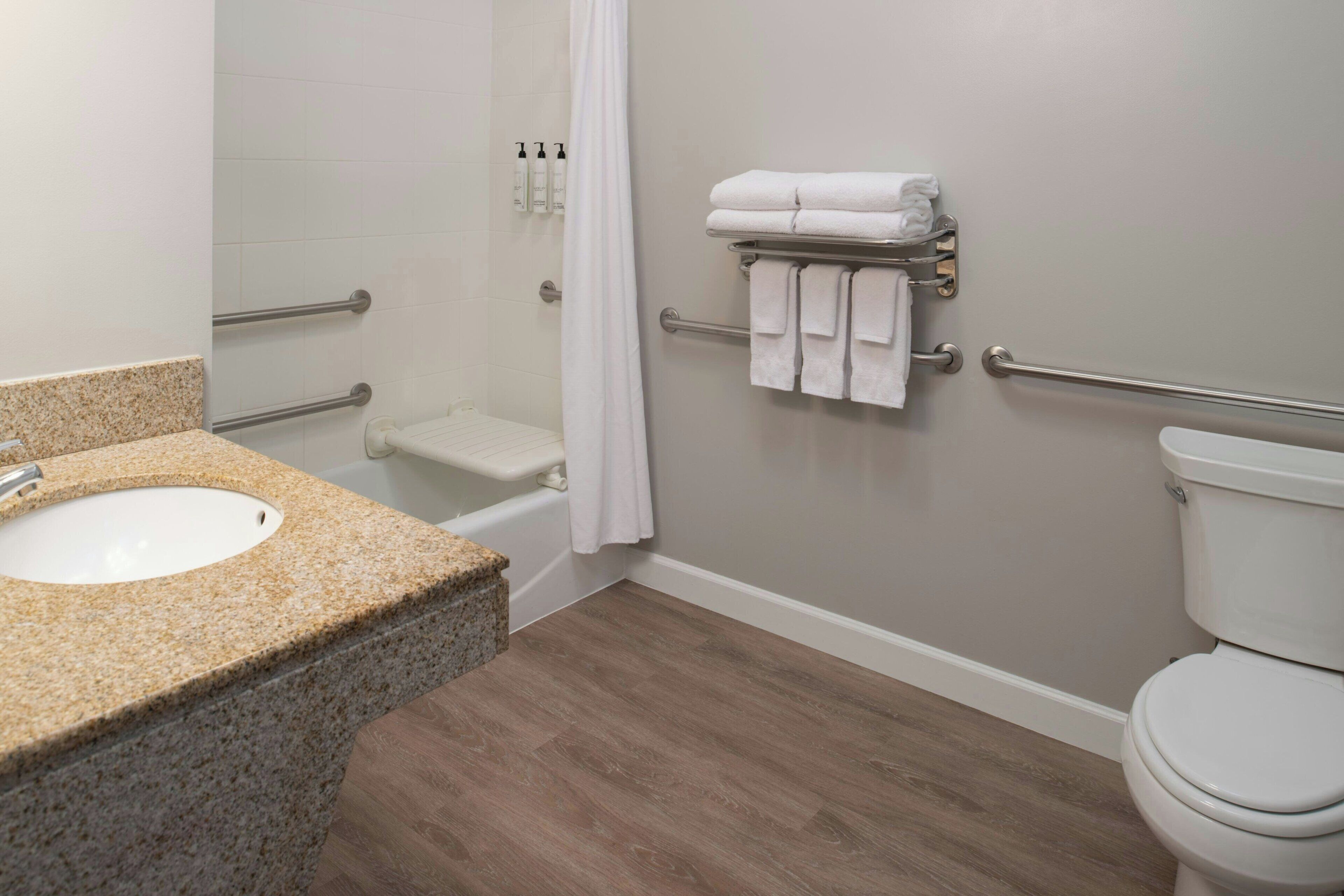 A bathroom with a granite countertop sink, a white toilet, a shower with a glass door, and a towel rack with folded towels.