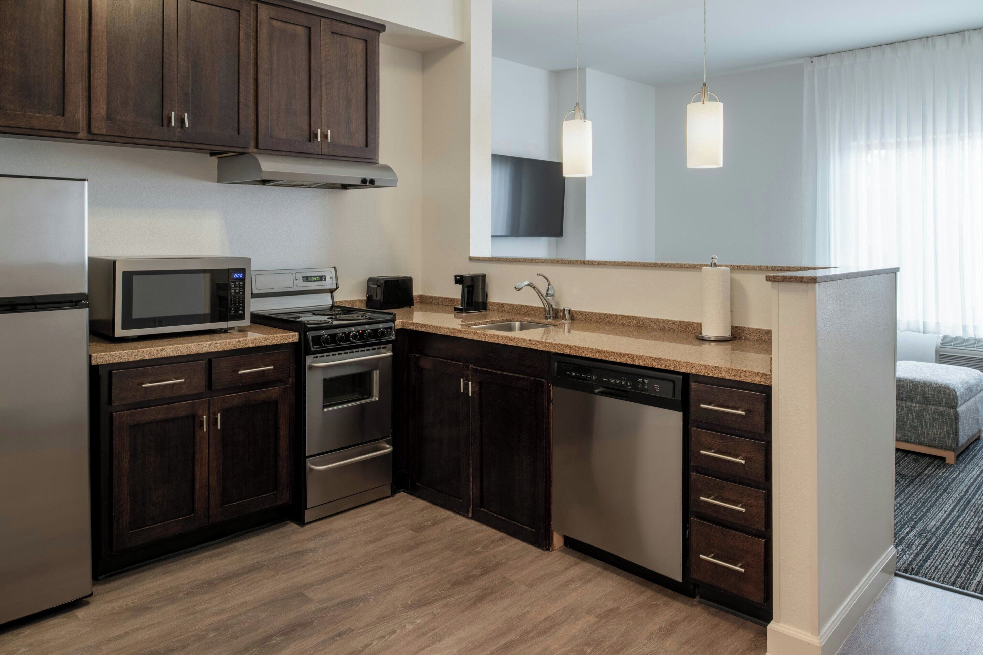 A modern kitchen with dark wood cabinets, stainless steel appliances, a granite countertop, and a large mirror above the sink.