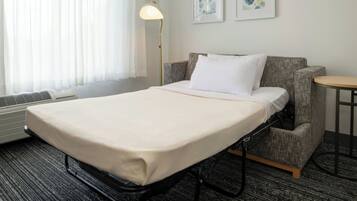 Une chambre d’hôtel avec un lit, une chaise, une petite table et une lampe.