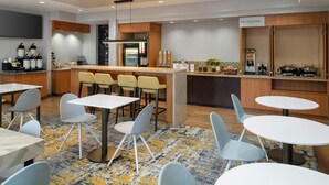 A modern kitchen with a breakfast bar, seating area with tables and chairs, and a 'Morning Break' sign.