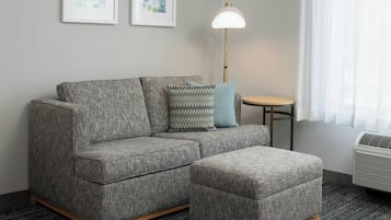 A gray sectional sofa with a matching ottoman, a small round table, a floor lamp, and two framed abstract artworks on the wall.