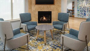 A modern lounge area with a fireplace, seating, and a large abstract wall art piece.