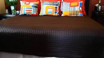 A hotel room with a large bed, a headboard with multiple pillows, a nightstand with a vase of flowers, and a carpet with a striped pattern.