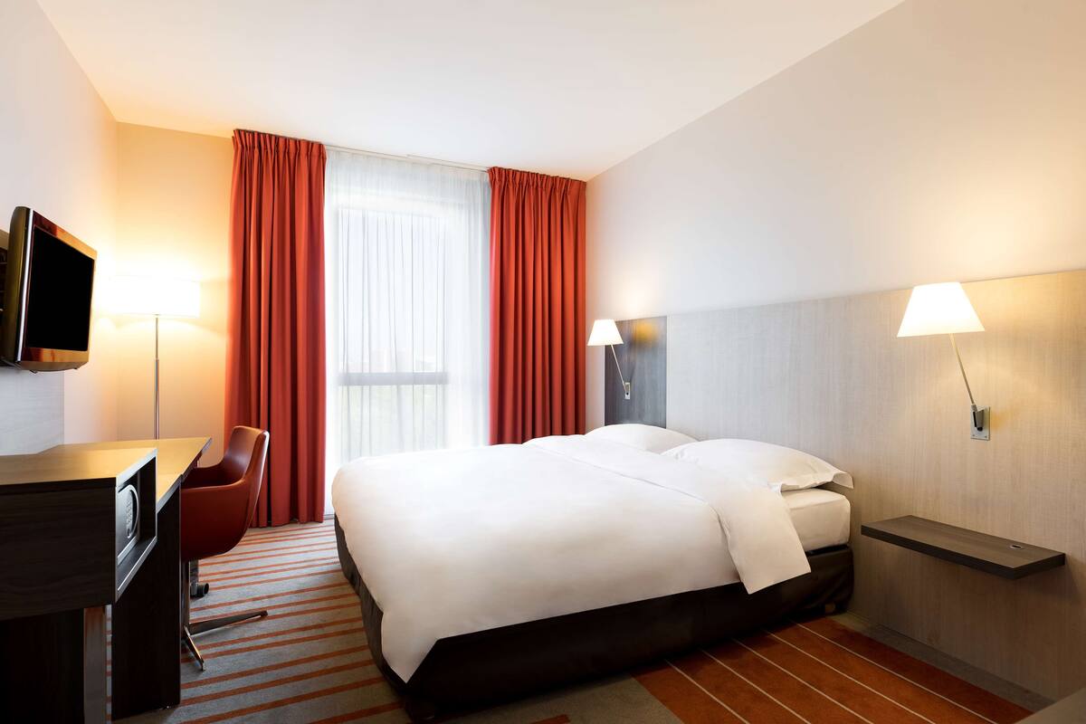 Habitación de hotel con cama, escritorio, silla, televisión y dos lámparas.