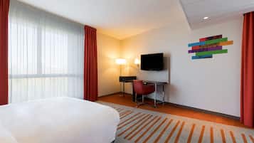 A hotel room with a bed, a desk, a chair, a TV, and a wall art piece.
