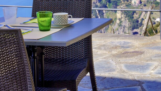A table with chairs and a green glass on a terrace overlooking a coastal view with mountains and a town in the distance. - Luna di Marzo (Volastra)