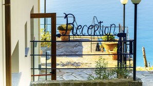 A reception gate with a sign, a stone-paved area with potted plants, and a view of the sea. - Luna di Marzo (Volastra)