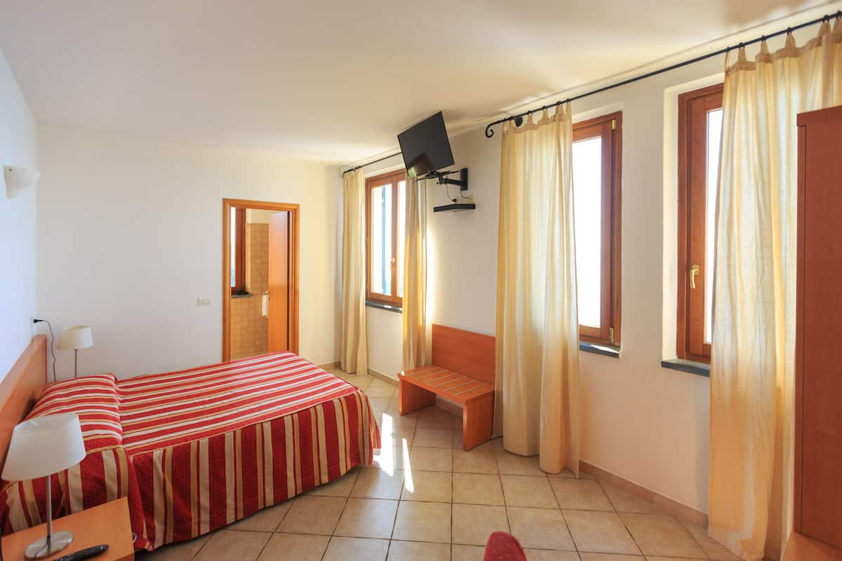 A hotel room with a bed, a bench, a TV mounted on the wall, and curtains on the windows.