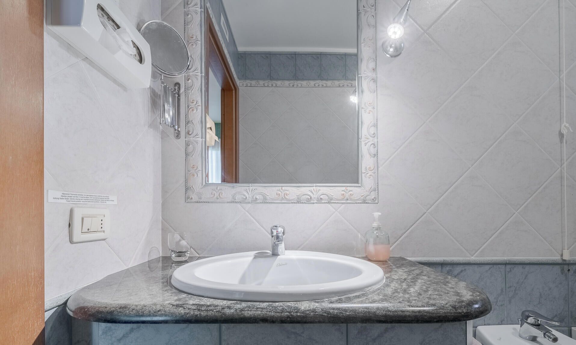 Un bagno con un lavandino bianco, uno specchio, un erogatore di sapone e un porta asciugamani.