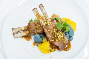 Un plato con chuletas de cordero, coliflor azul y puré amarillo.