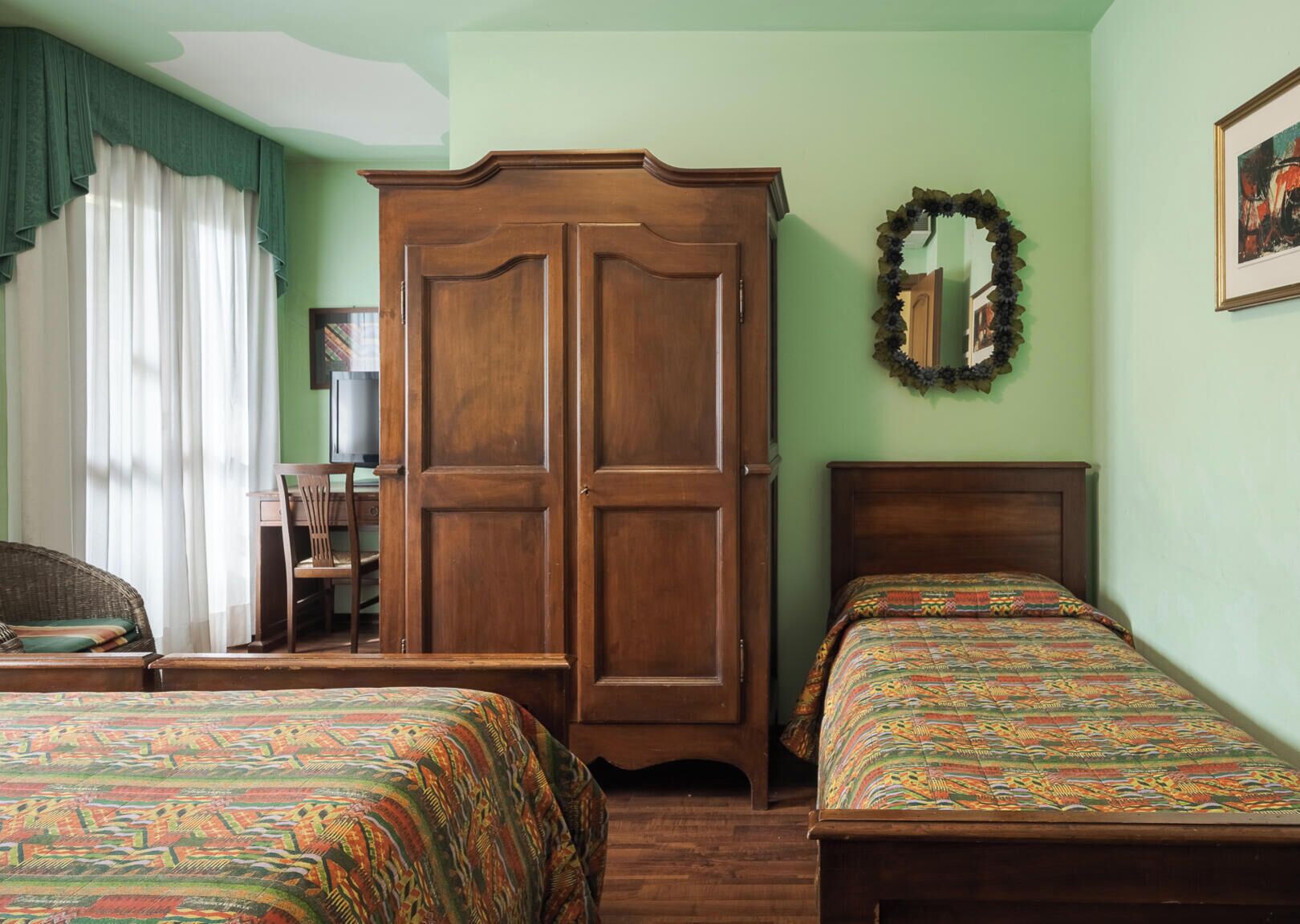 Una habitación con dos camas, un armario de madera, un escritorio con silla y un espejo en la pared.