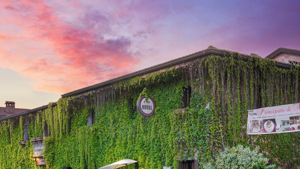A hotel with a sign indicating it is a hotel, ivy-covered walls, and a banner with text. - Principato di Ariis (Rivignano Teor)