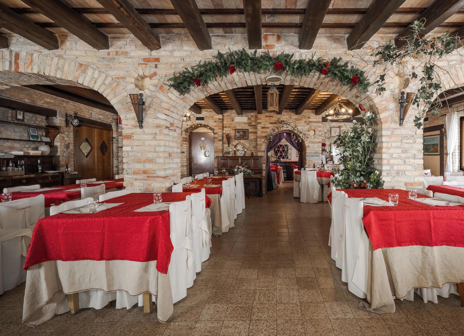 A restaurant with brick walls, wooden beams, and tables set with red tablecloths.