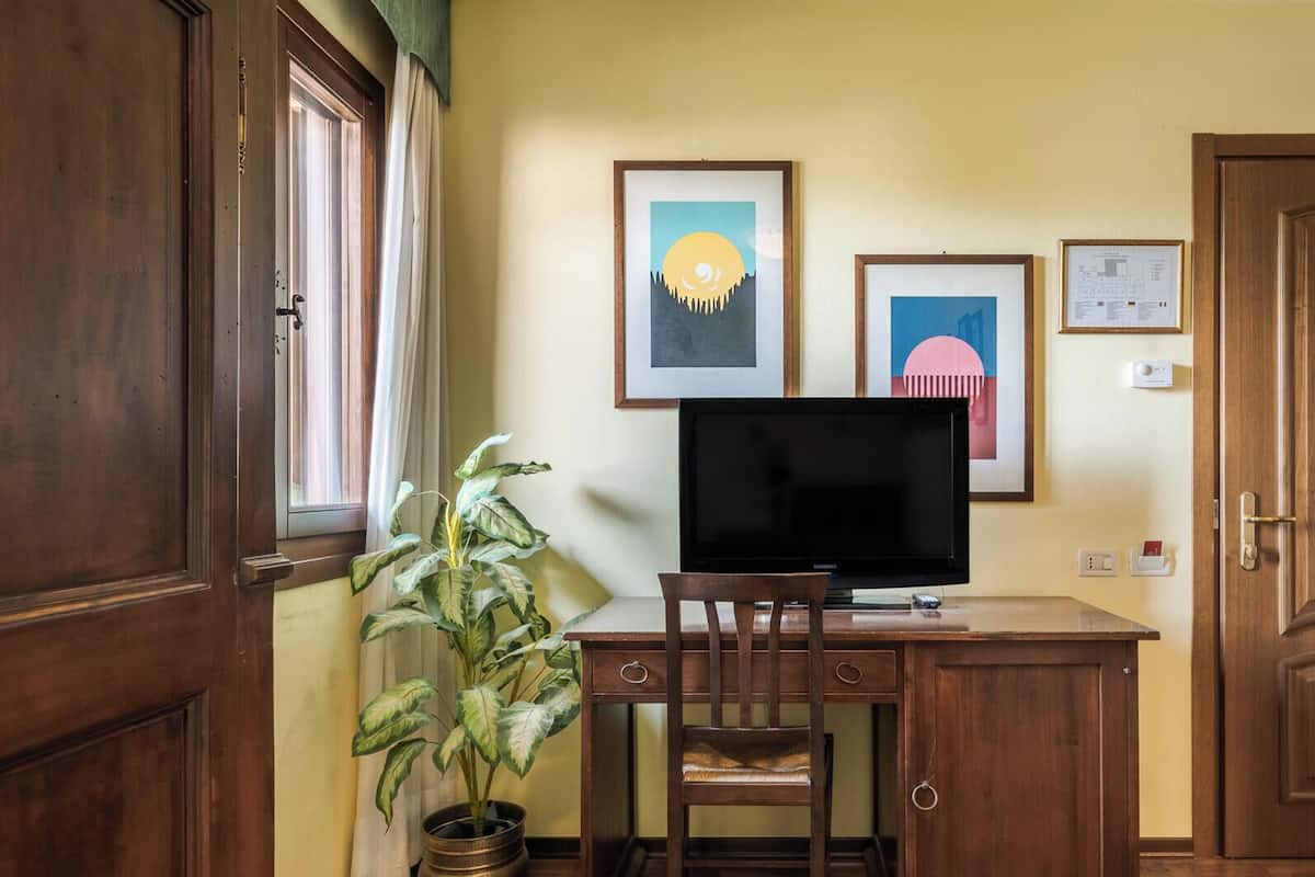 A room with a wooden desk, a television, a chair, a potted plant, and framed pictures on the wall.
