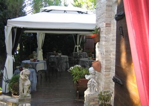 A covered patio area with tables and chairs, stone statues, and potted plants. - Principato di Ariis (Rivignano Teor)