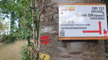A directional sign attached to a tree with a QR code, indicating GR 121 Brussels and GR 512 routes.