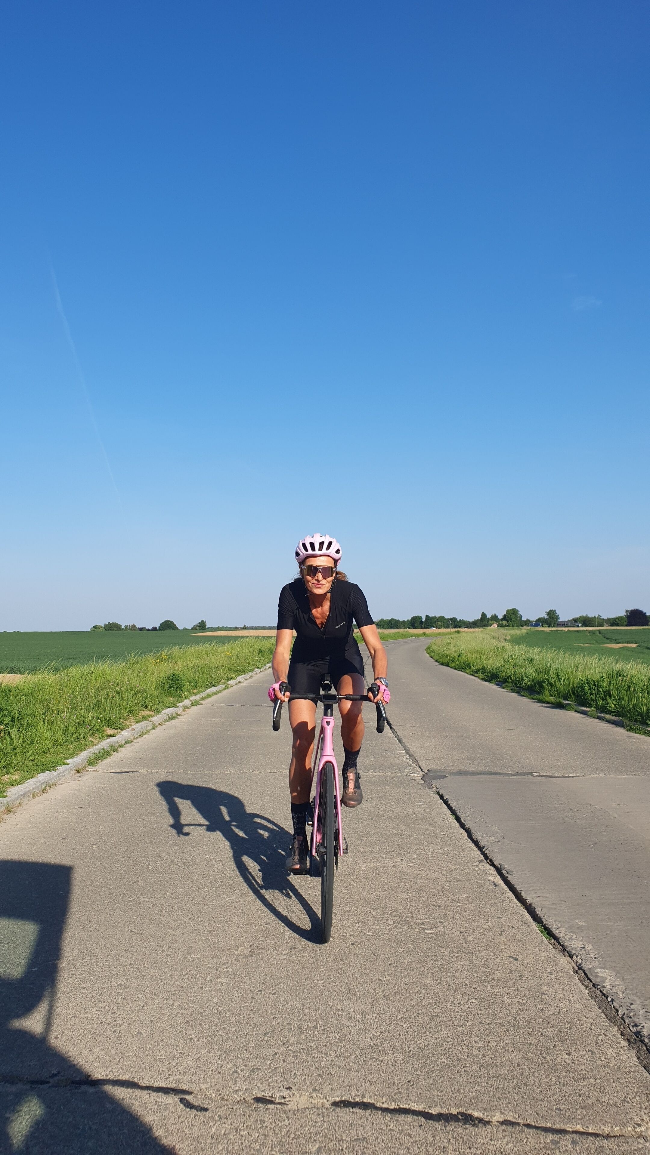 A person riding a pink bicycle on a paved road with grassy fields on either side.