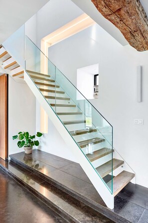 Un escalier moderne avec des rampes en verre et des marches en bois, menant à un deuxième étage.