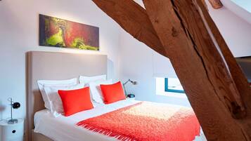 Une chambre à coucher avec un lit, du linge de lit blanc, des oreillers rouges, un plaid rouge, une table de chevet avec une lampe et un tableau accroché au mur.