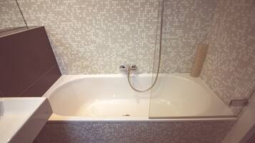 Une salle de bain moderne dotée d’une grande baignoire, d’un espace douche et d’un mur carrelé.