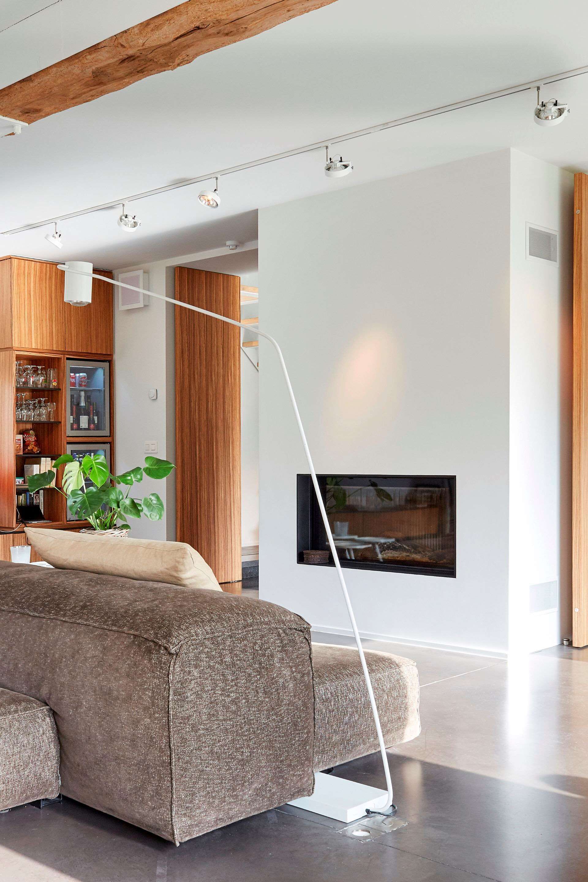 Una sala de estar moderna con un sofá, una lámpara de pie, una chimenea y un aparador de madera con puertas de vidrio.