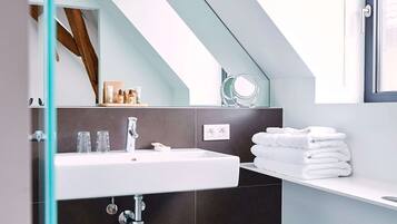 Een moderne badkamer met een douchecabine van glas, een witte wastafel, donker betegelde wanden en een raam met uitzicht.