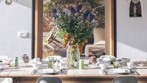 A dining area with a table set for four, surrounded by two chandeliers, and a view of a garden through an open doorway. - Park 7 (Huldenberg)