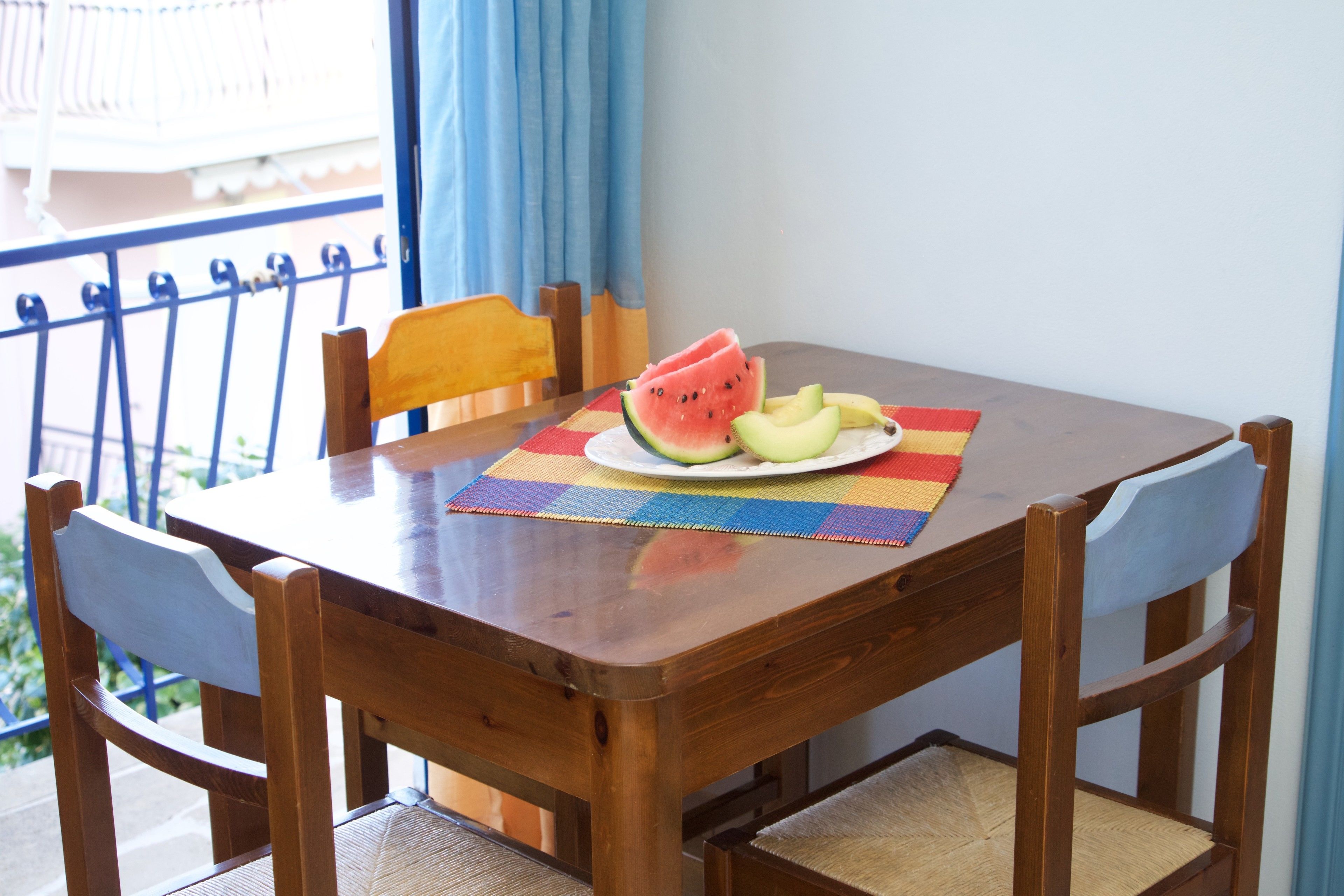 Una mesa de madera con un mantel individual colorido, dos sillas y un plato con sandía y melón en rodajas.