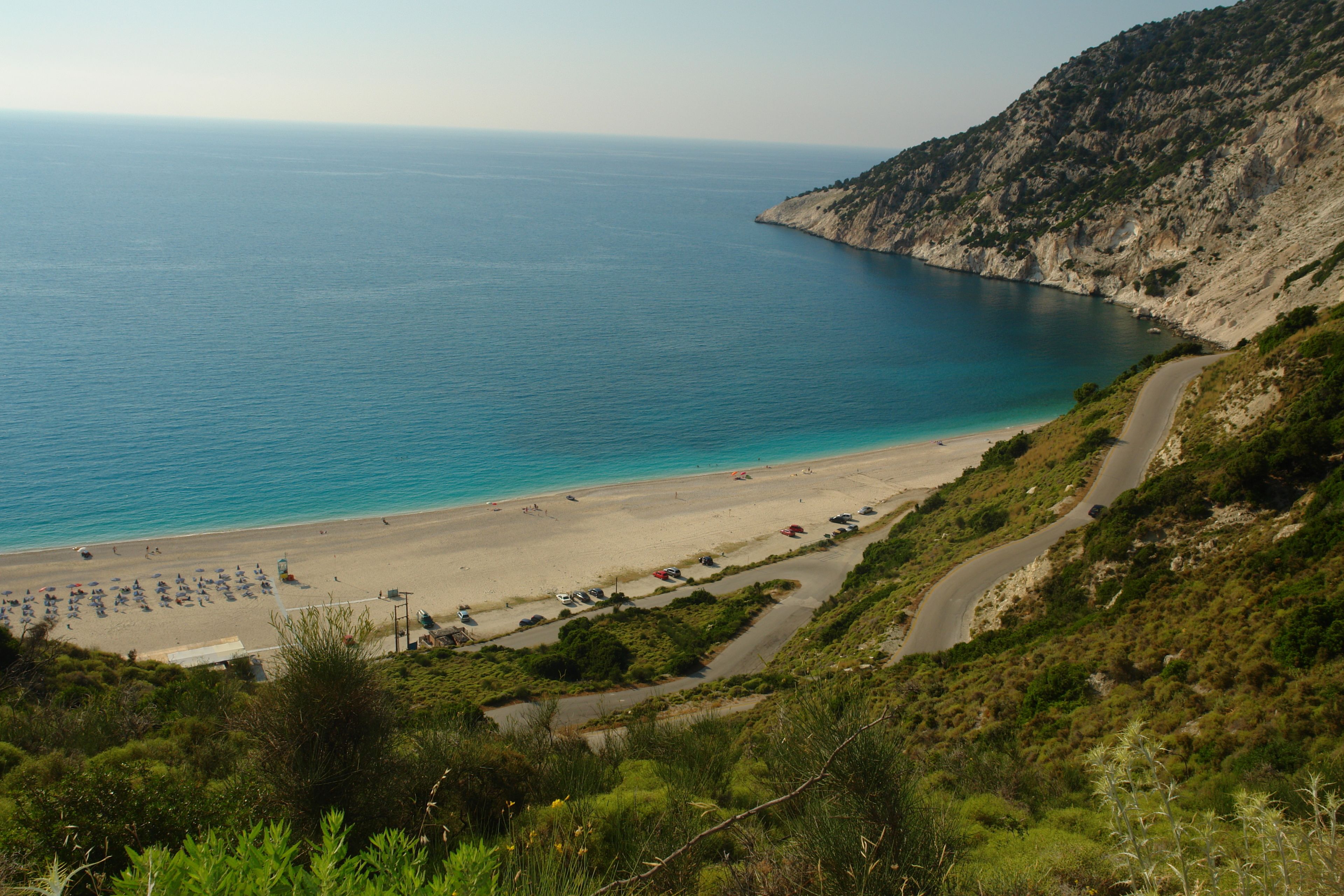 A coastal road leading to a beach with parked cars and umbrellas.