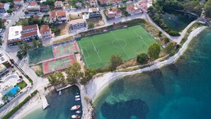 Vista aérea de un pueblo costero con un campo deportivo, edificios residenciales y un puerto deportivo.