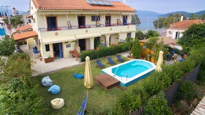 Un edificio de dos pisos con piscina, mobiliario exterior y vista al mar.