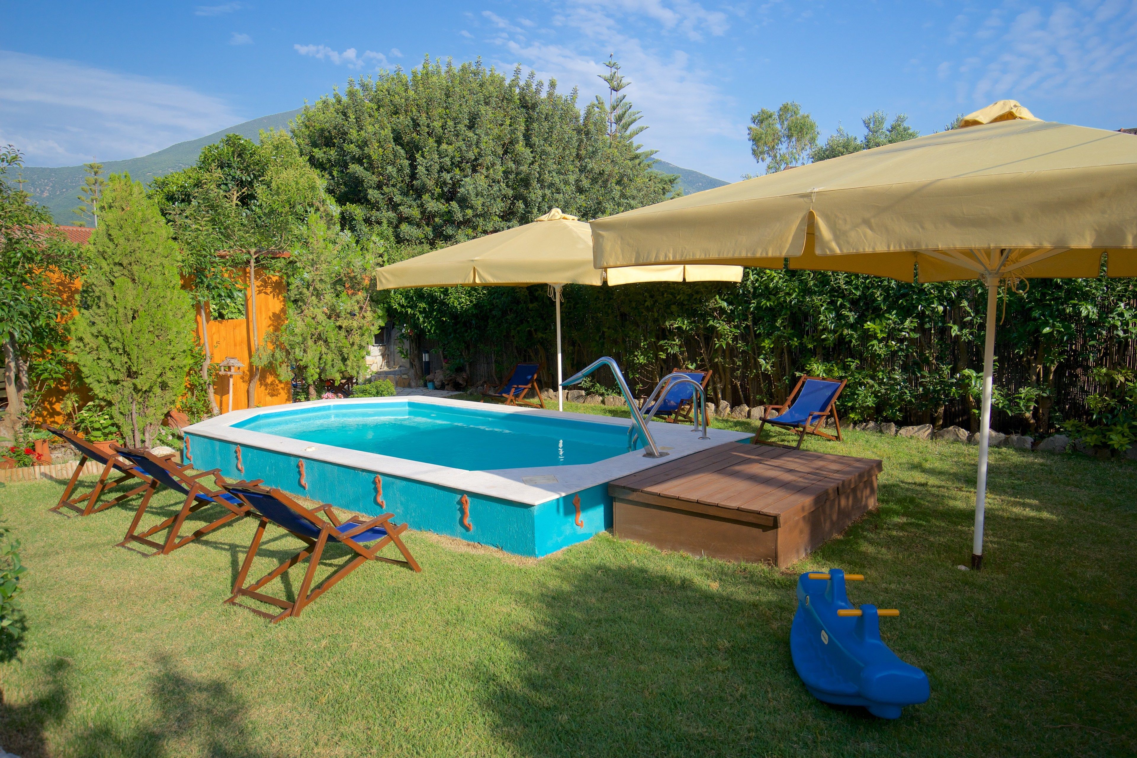 A swimming pool with lounge chairs and umbrellas, surrounded by greenery and mountains in the background.