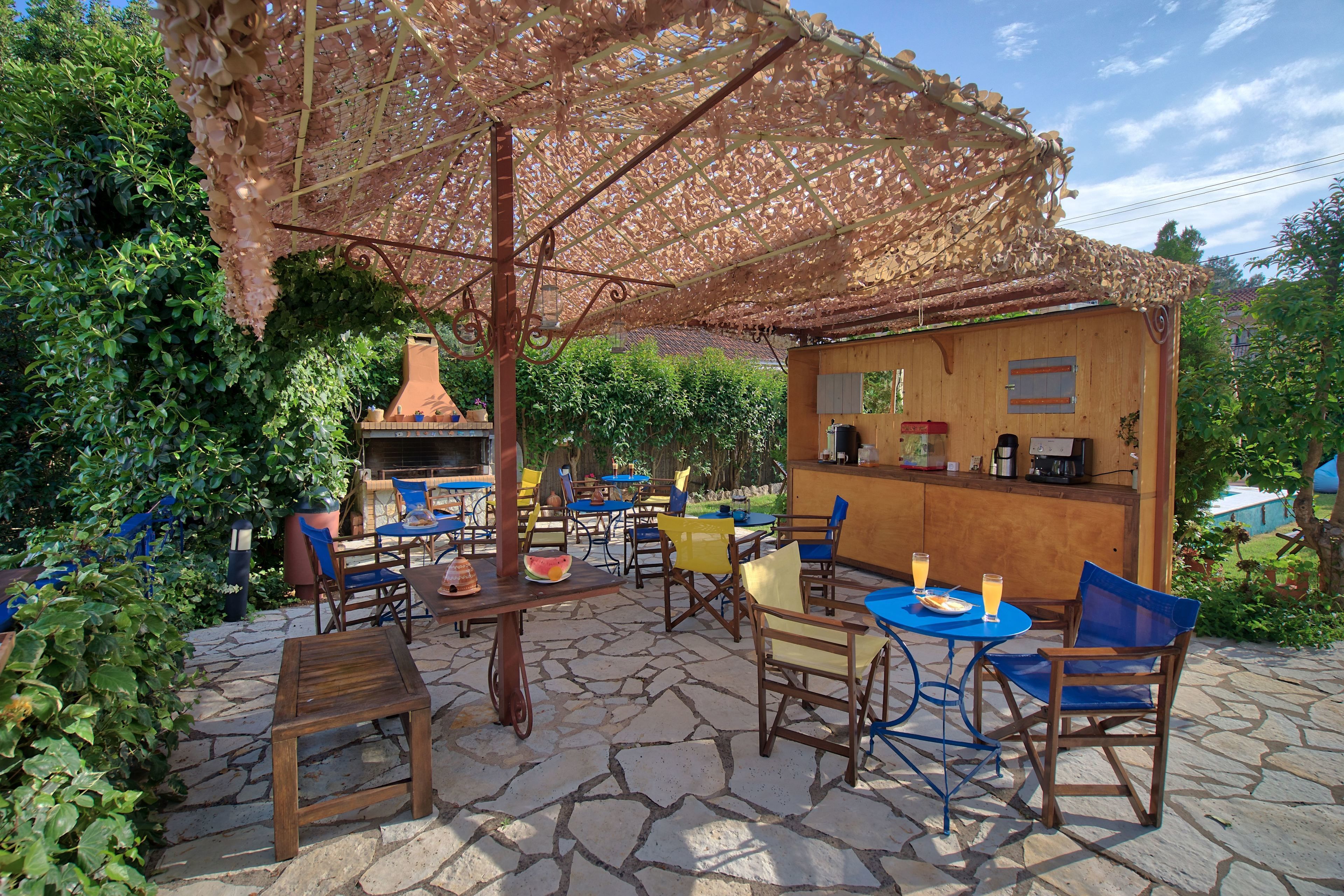 An outdoor patio with stone flooring, wooden tables and chairs, a barbecue grill, and a small bar area.