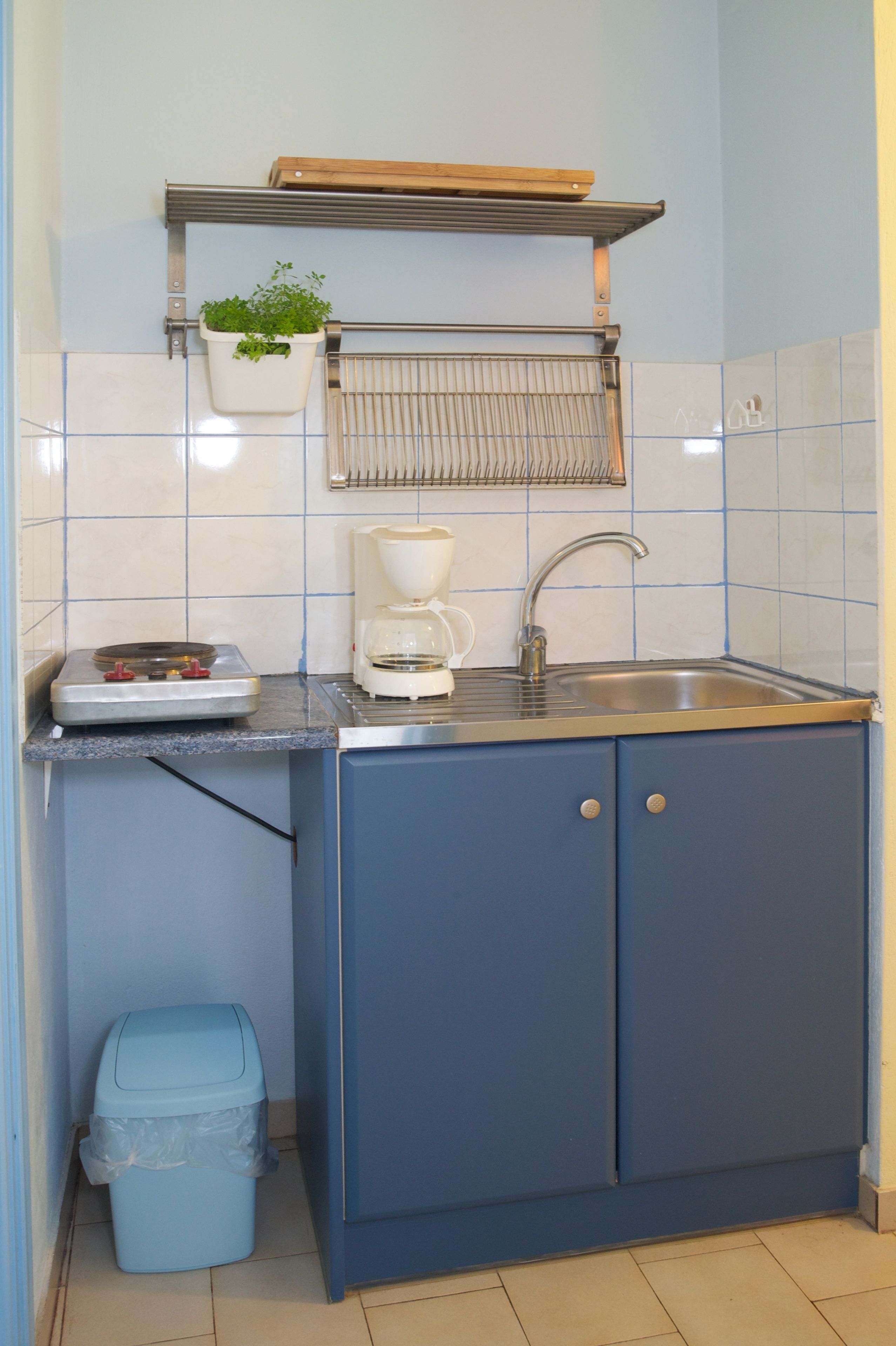 Cocina compacta con un lavamanos, una cafetera y un pequeño cubo de basura.