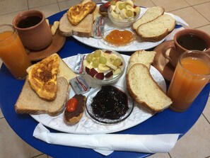 Bandeja de desayuno con tostadas, mermelada, un bol de fruta y dos vasos de jugo de naranja.