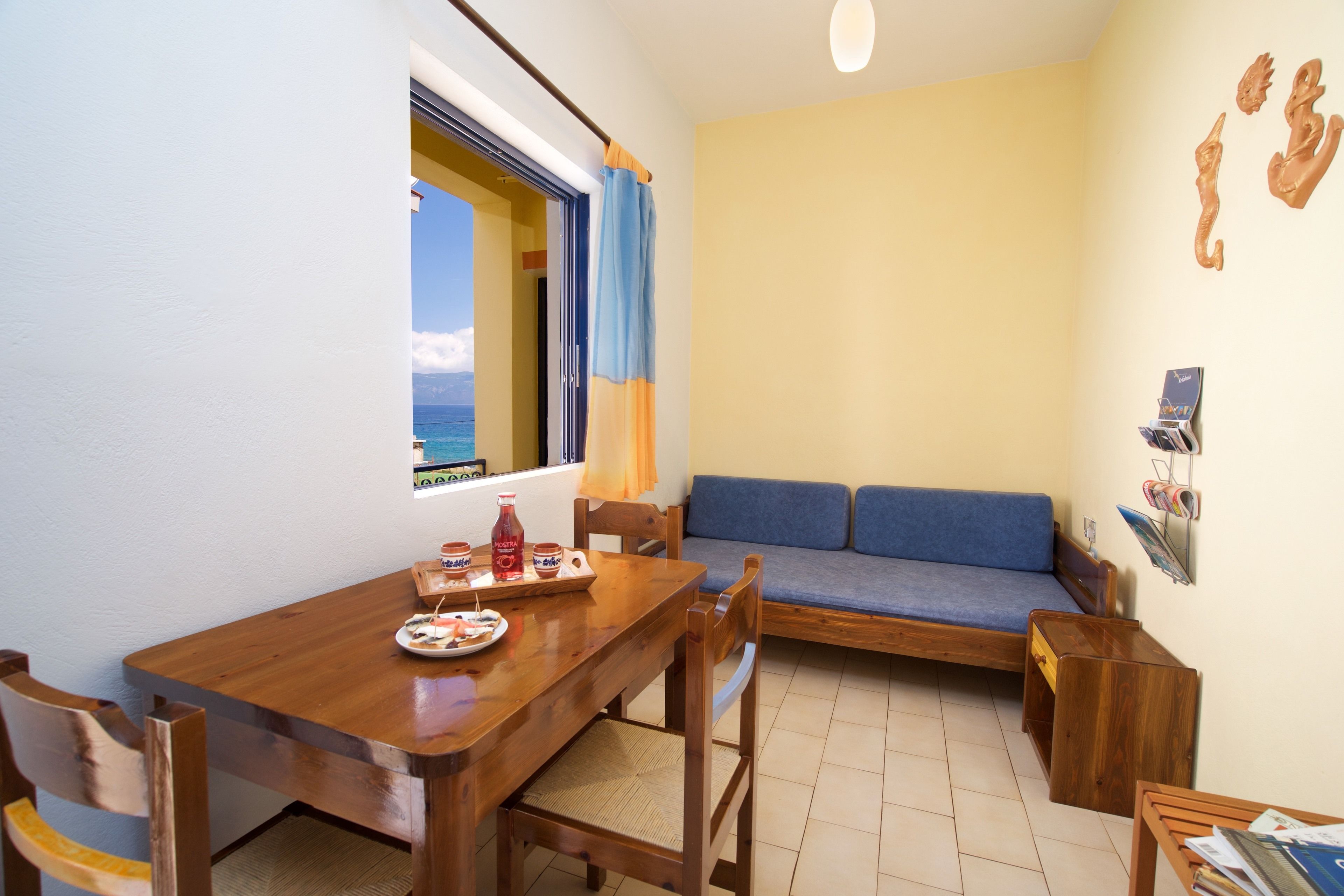 A compact living space with a wooden dining table, a sofa, and a small seating area. A window provides a view of the ocean.
