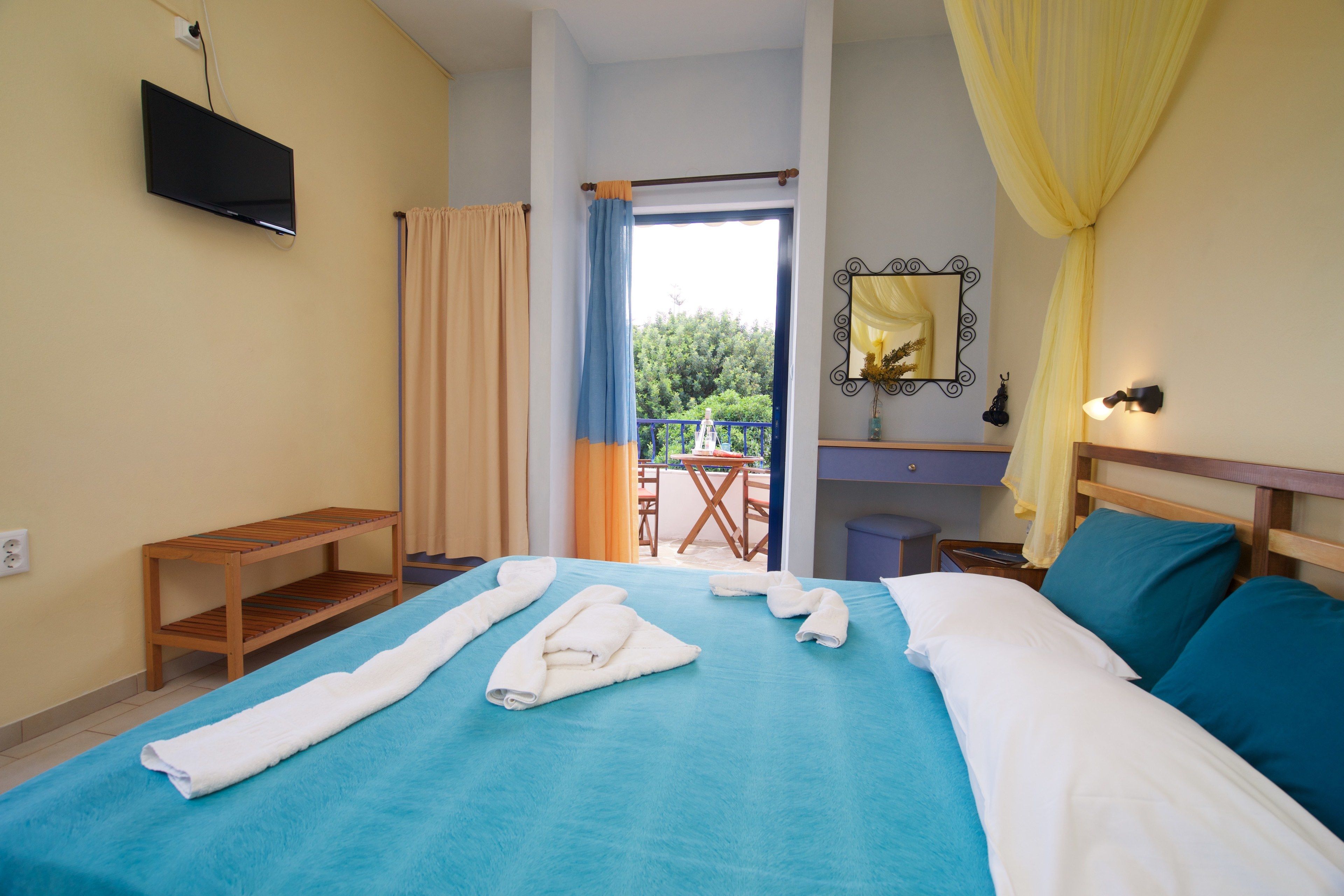 Ein Hotelzimmer mit Bett, Fernseher, einem kleinen Tisch und einem Balkon mit Blick auf Gr ünflächen.