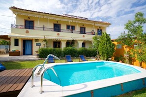 Un edificio de dos pisos con una piscina, un balcón con barandas azules y una terraza de madera.